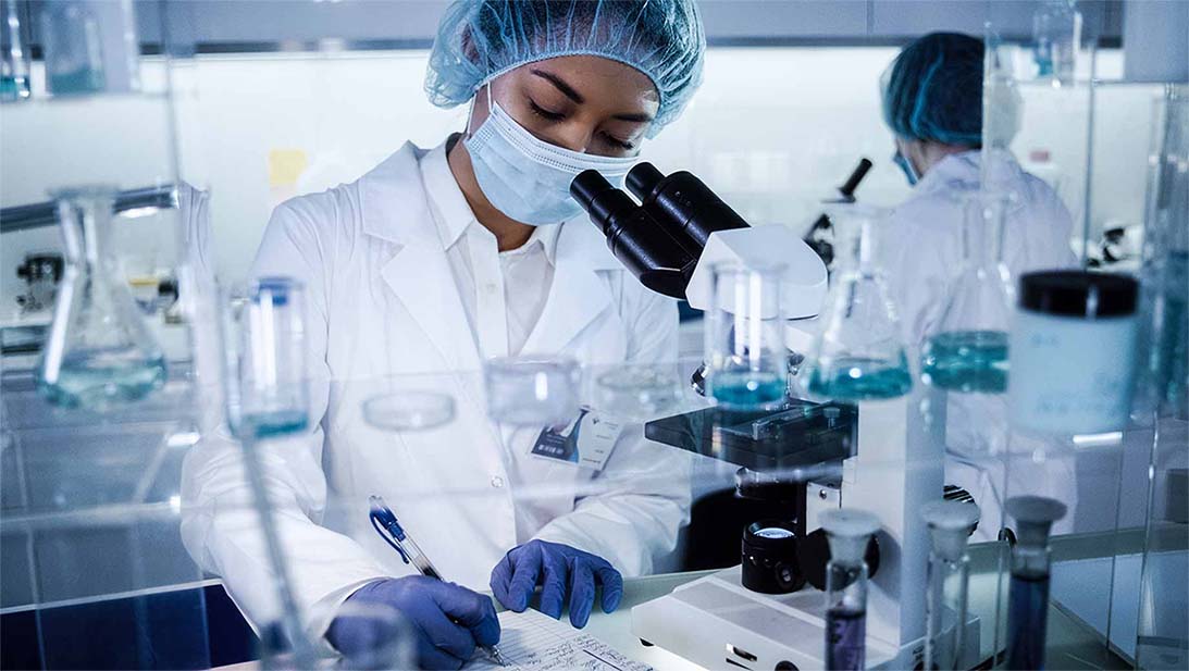 A scientist writing down notes near a microscope